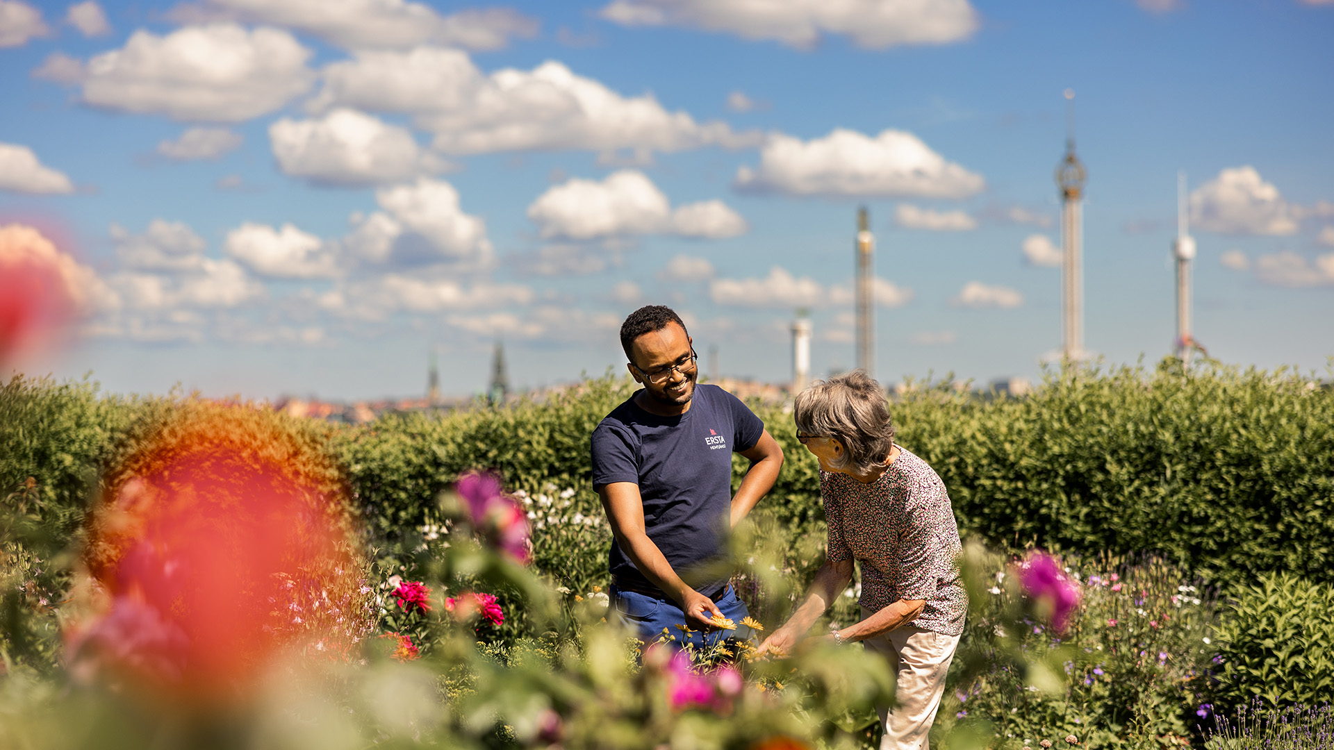 en medarbetare från ersta hemtjänst står i en trädgård med blommor tillsammans med en äldre kvinna