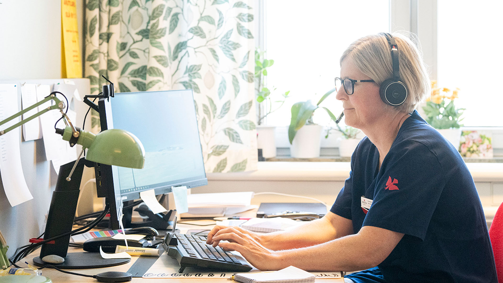 Kvinlig sjukvårdspersonal sitter vid dator med headset